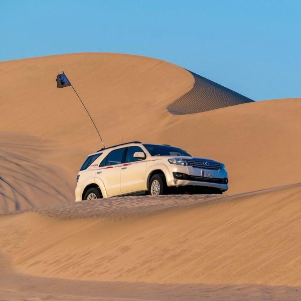 Modern off road car driving along desert sandy dunes against blue sky