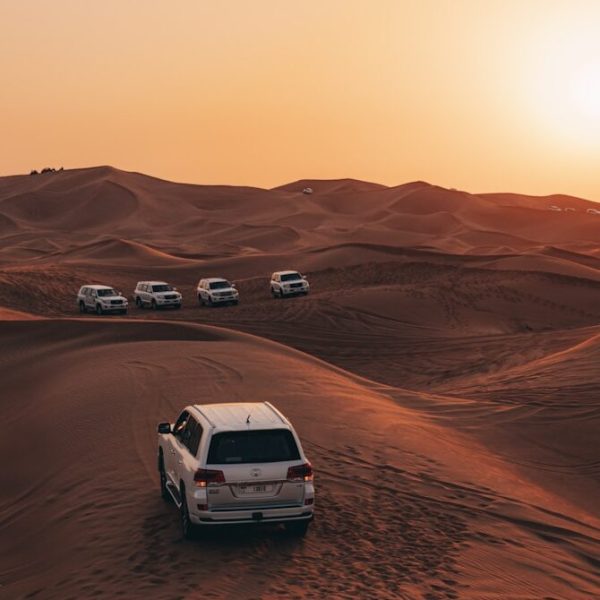 a white car driving through the desert at sunset